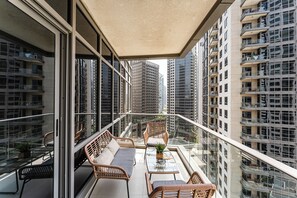 Ein Balkon mit Korbmöbeln, einem Glastisch und Blick auf hohe Gebäude.