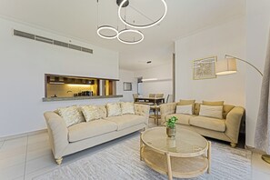 Ein modernes Wohnzimmer mit einem beigefarbenen Sofa, einem runden Couchtisch und einem durch eine offene Tür einsehbaren Küchenbereich.