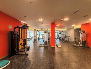 Ein Fitnessraum mit verschiedenen Trainingsgeräten, einer Spiegelwand und einer roten Säule.