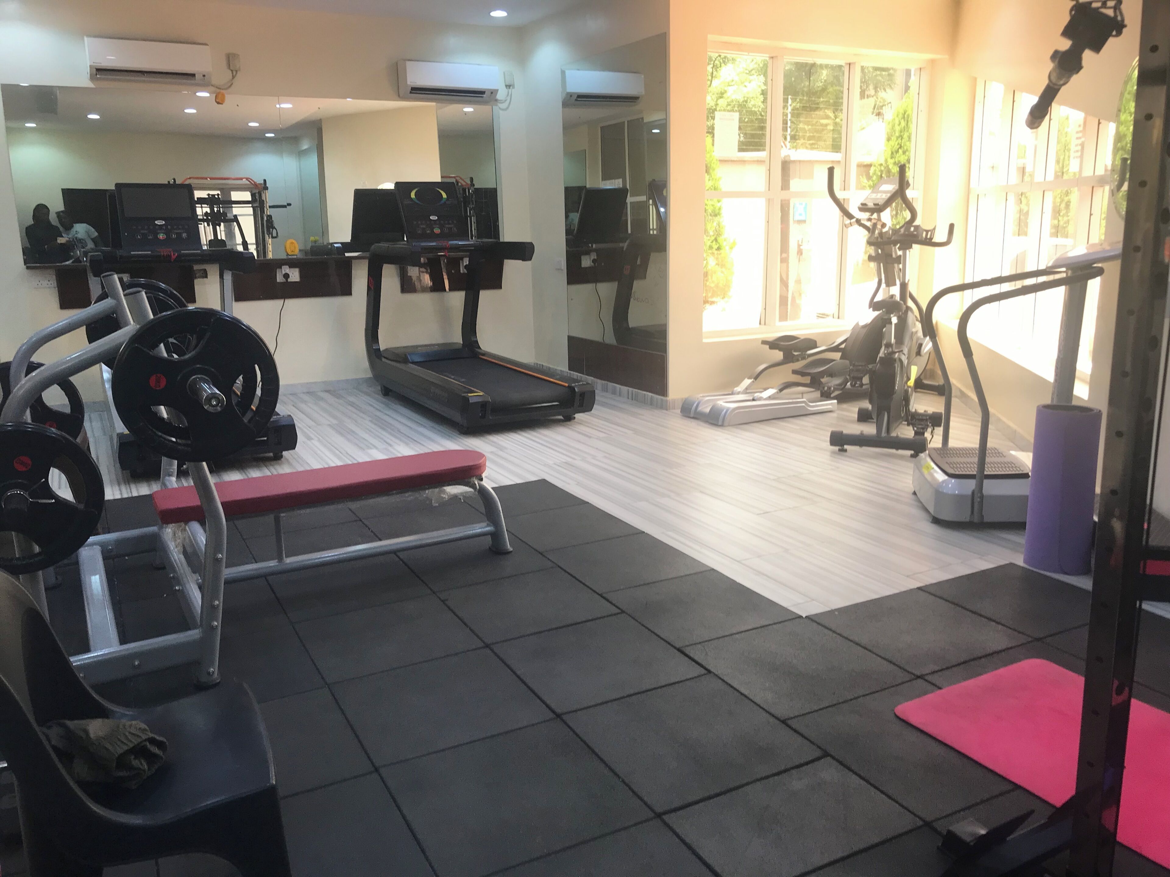 Uma academia com esteiras, aparelhos de musculação e um banco vermelho.