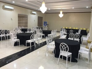 Un salón de conferencias con varias mesas y sillas, unidades de aire acondicionado y candelabros.