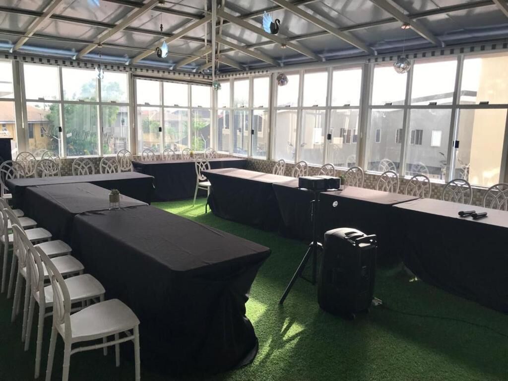 A covered outdoor area with tables and chairs, large windows, and a green carpet.
