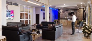 A hotel lobby with leather sofas, a reception desk, and a television displaying news. - ADJ Royalty Hotel & Suites (Benin City)