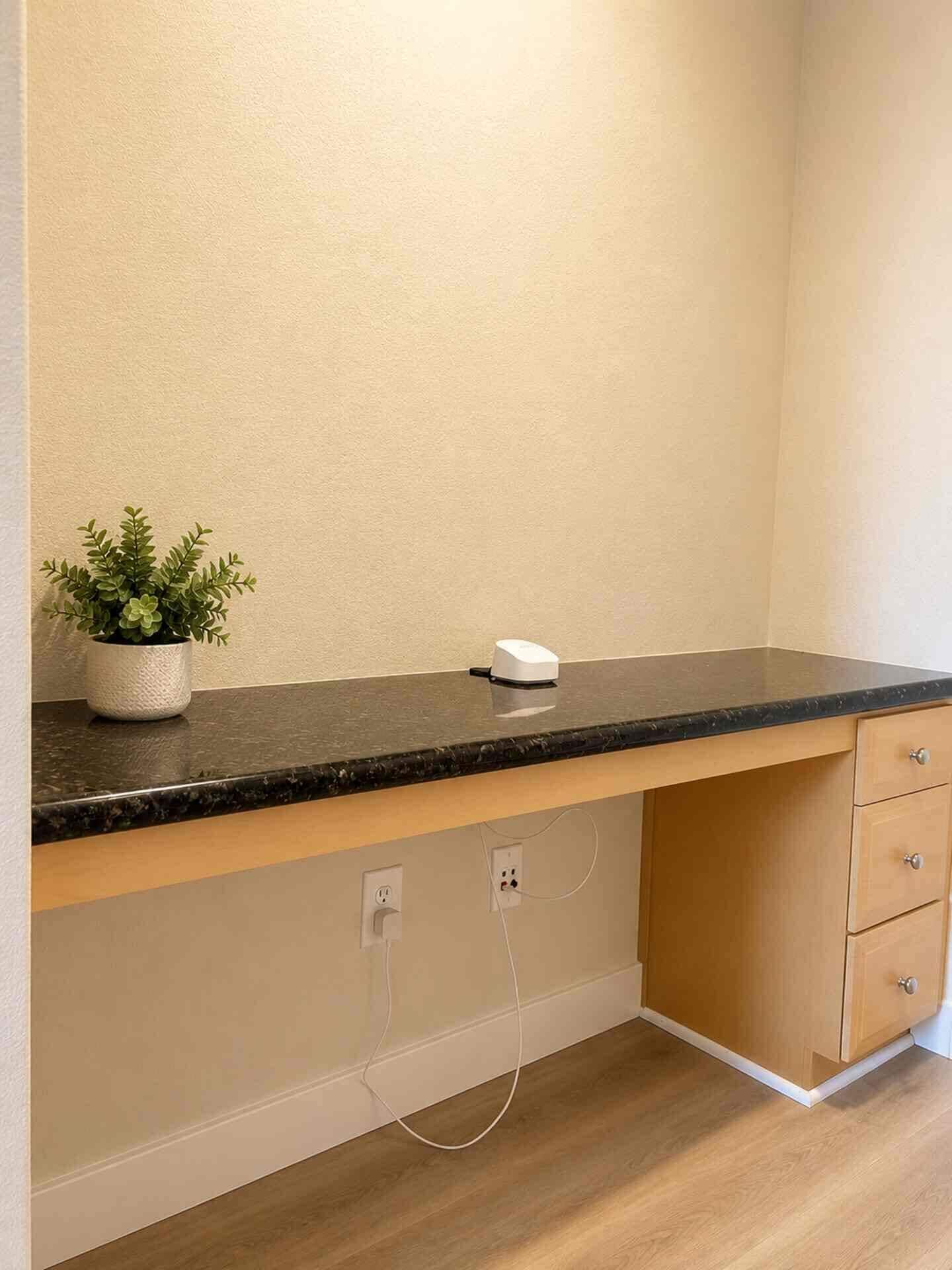 Una cucina con un piano di lavoro nero, una pianta in vaso, un dispositivo bianco, mobili in legno e un pavimento in legno.