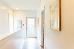 Un couloir avec une porte au fond, des œuvres d’art encadrées accrochées aux murs et une fenêtre sur le côté gauche.