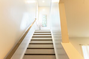 Un escalier muni d’une rampe menant à une pièce où un tableau est accroché au mur.