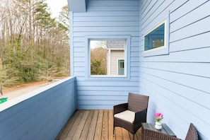 Un mur extérieur bleu avec une fenêtre et une chaise en osier sur une terrasse en bois.