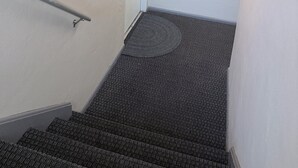 En trappe med gelænder, en dør med skilt 'WELCOME' og et overvågningskamera.