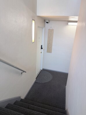 Una escalera con barandilla, una puerta con un letrero de 'WELCOME' y una cámara de seguridad.