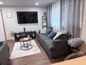 Una sala moderna con un sofá gris, una mesa de centro, un televisor de pantalla plana y una estantería con adornos.