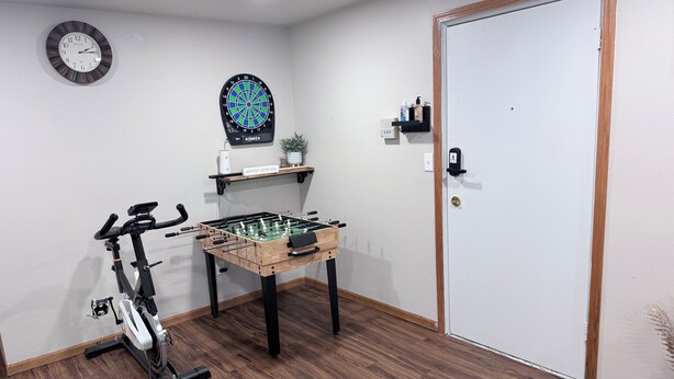 Et værelse med et bordtennisbord, motionscykel, dartskive og en dør.