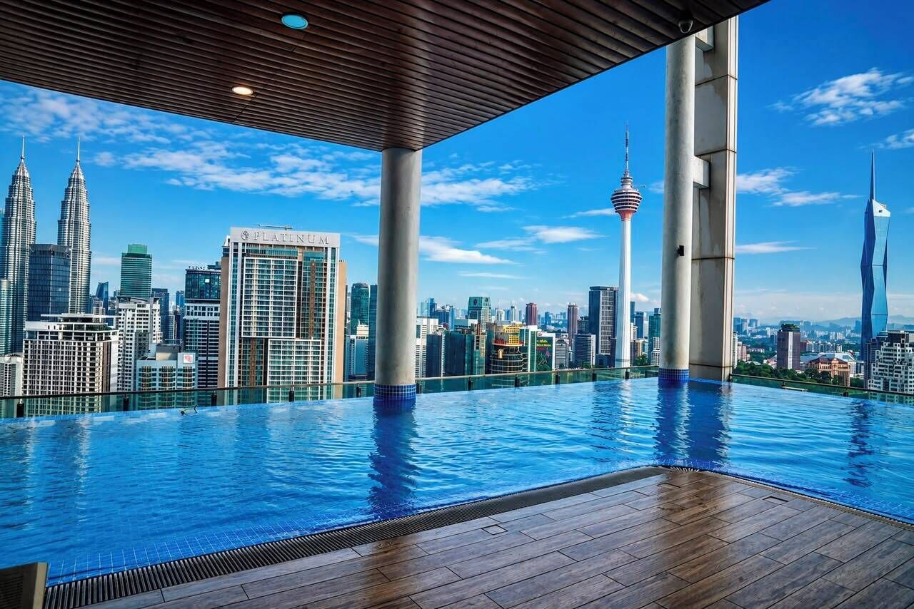 Una piscina infinita con vistas al horizonte urbano, incluyendo las Torres Petronas y una torre con un mirador circular.