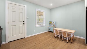 A room with a wooden floor, a white door, a window with blinds, a play kitchen, and a table with chairs. - Adorable 3-bedroom house with in minutes I-40 and half a mile from 540 (Fort Smith)