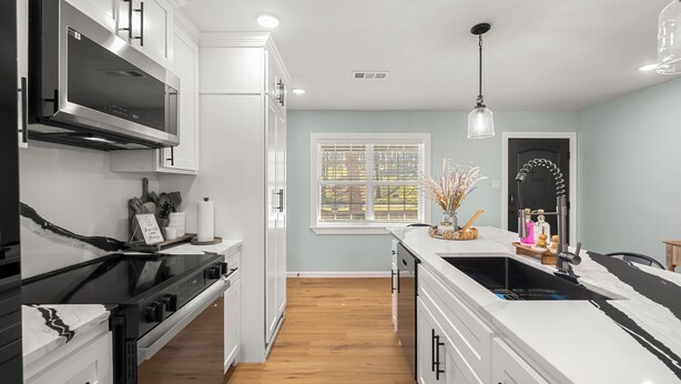 A modern kitchen with white cabinetry, a black stove, and a window with blinds. - Adorable 3-bedroom house with in minutes I-40 and half a mile from 540 (Fort Smith)