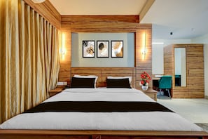 A modern bedroom with a wooden headboard, a bed with white and black bedding, a nightstand with a phone, and a wall-mounted light fixture. - Classic Palette Hotel and Resort (Cuttack)