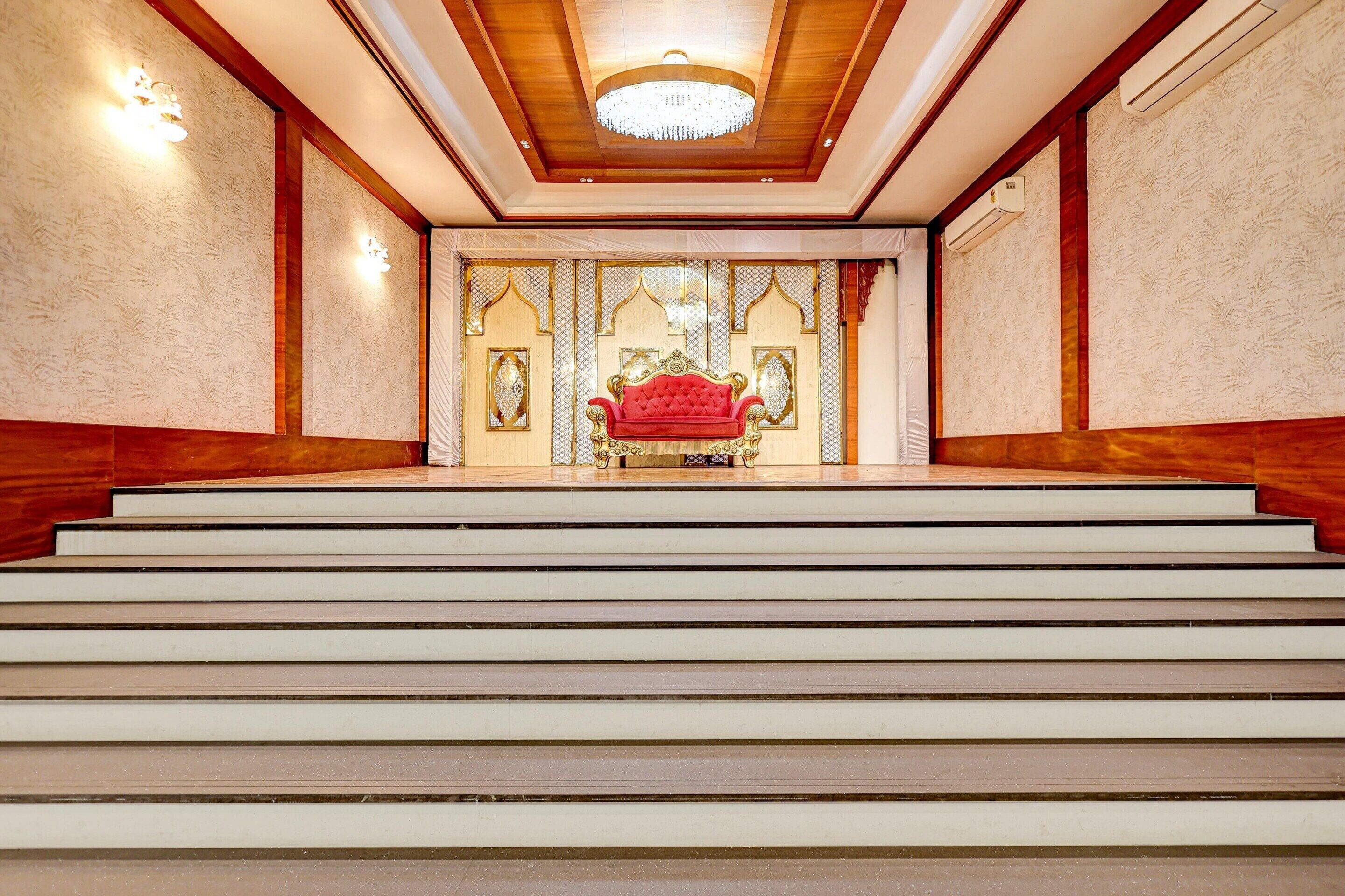 A grand staircase leading to a room with a red upholstered chair and ornate decor.