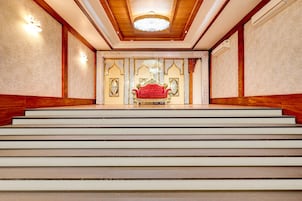A grand staircase leading to a room with a red upholstered chair and ornate decor.