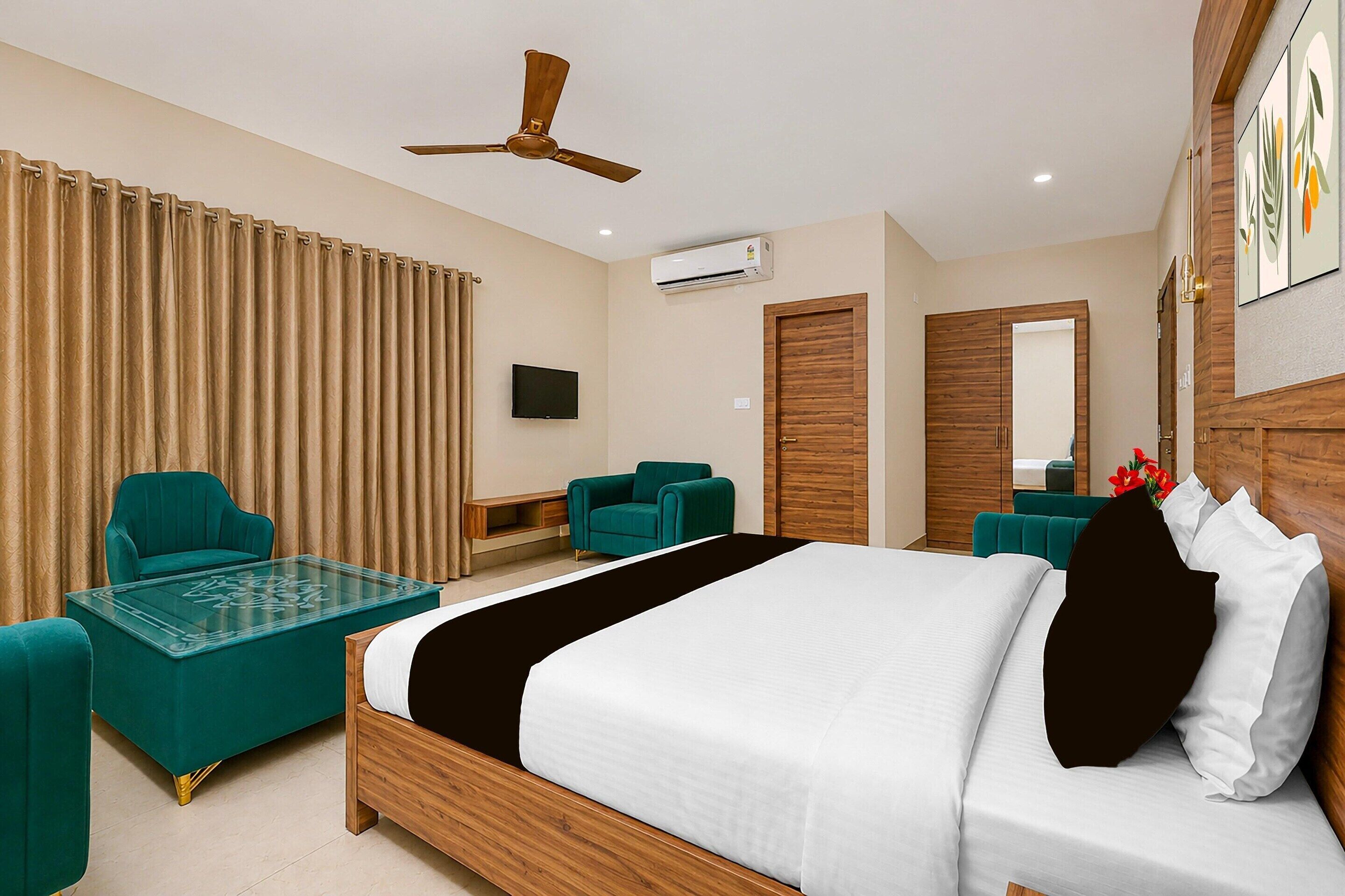 A hotel room with a bed, two chairs, a table, a ceiling fan, an air conditioning unit, and a television.