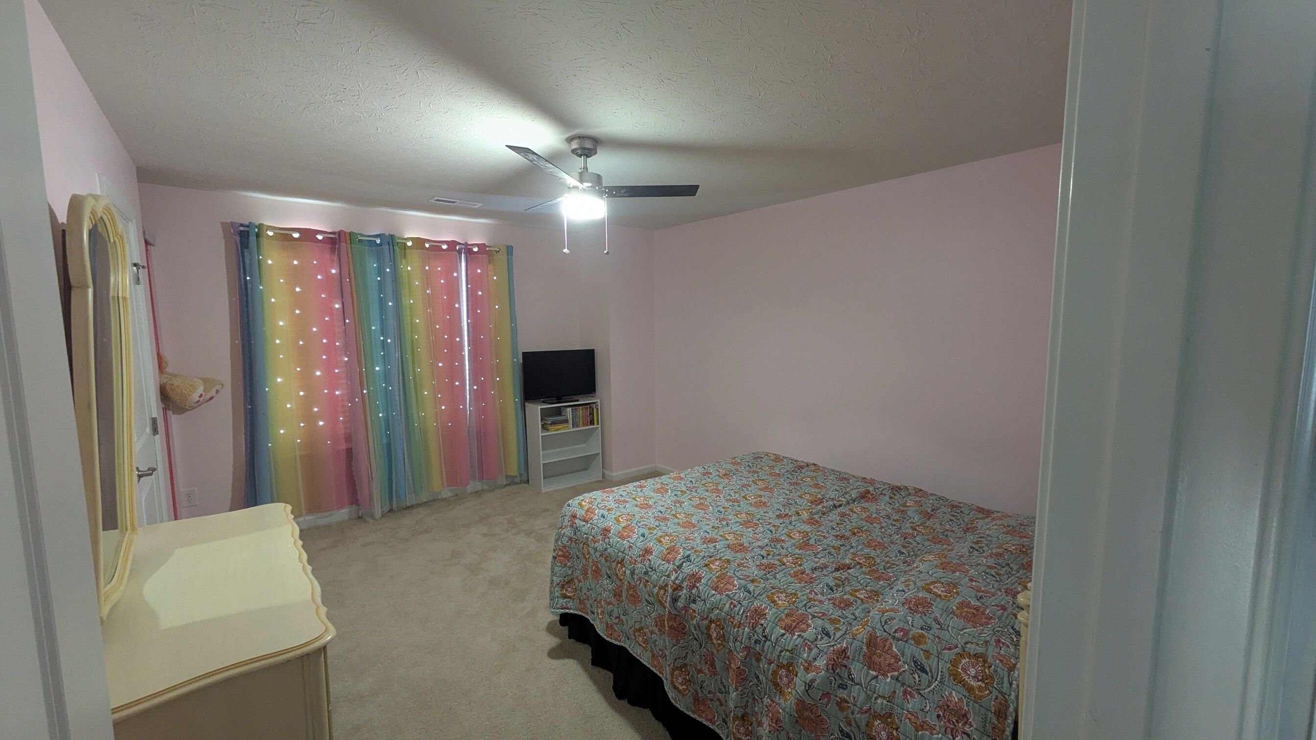 A bedroom with a bed, a dresser, a television on a stand, and a ceiling fan.