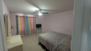 A bedroom with a bed, a dresser, a television on a stand, and a ceiling fan.
