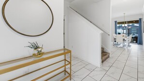 A modern interior with a staircase, a dining area, and a hallway leading to a room with a large window. - Family Friendly Home, Private Pool, Near Disney (Kissimmee)