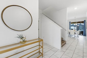 A modern interior with a staircase, a dining area, and a hallway leading to a room with a large window.