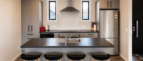 Una cocina moderna con una isla central, electrodomésticos de acero inoxidable y taburetes de bar.
