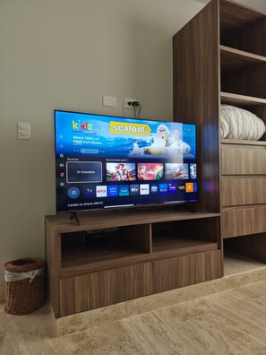 A flat-screen TV mounted on a wooden entertainment center with a digital display of a streaming service. - Modern apartment located in Aldea Zama with a pool, gym, and green spaces. (Tulum)