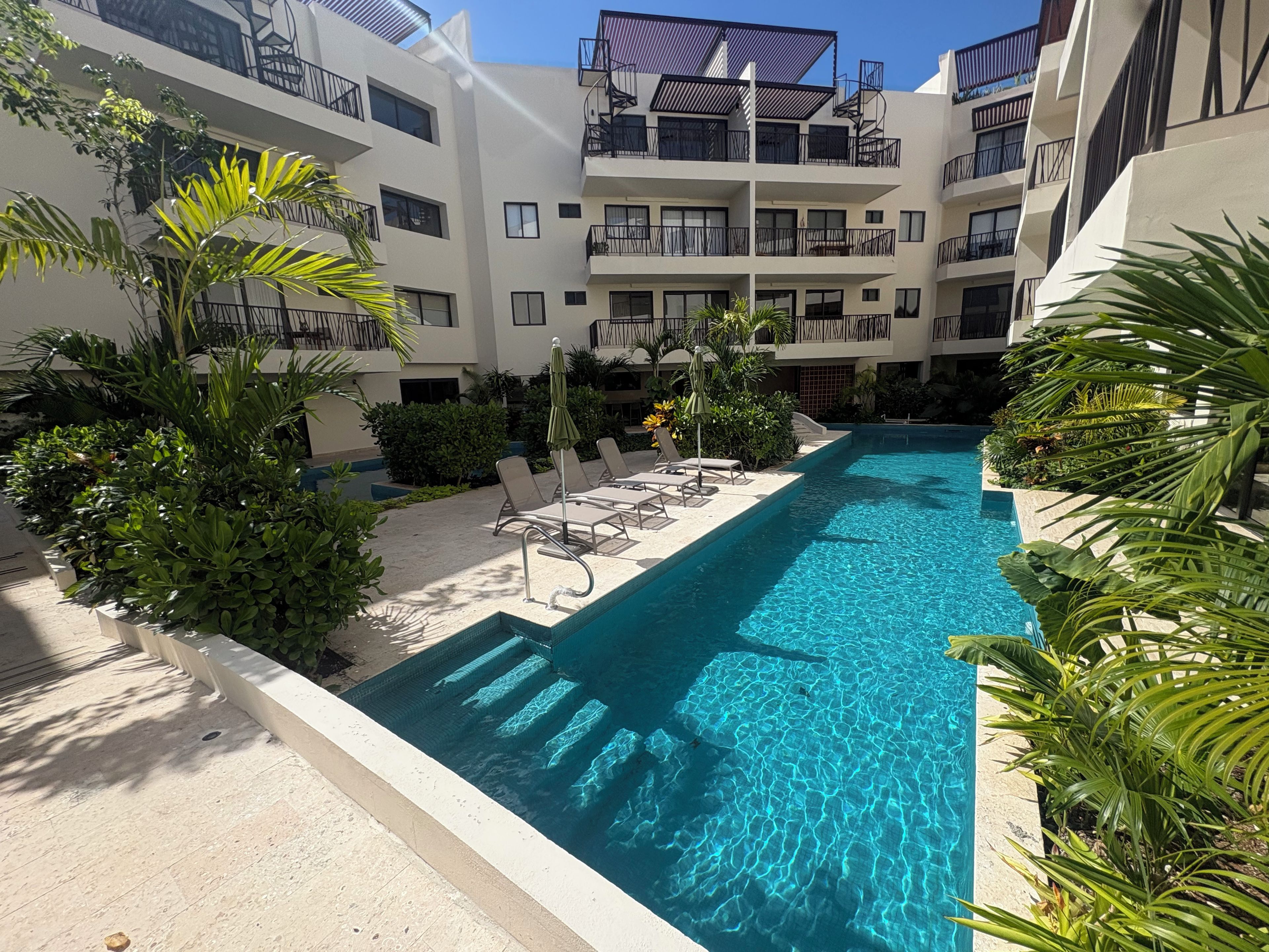 A swimming pool with lounge chairs and a multi-story building with balconies.