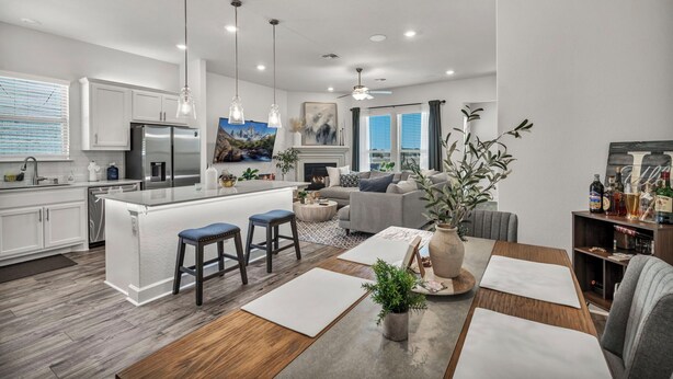 A modern kitchen with a central island, bar stools, a dining area with a wooden table, and a living room with a sofa and a fireplace. - Modern 4-bedroom Family Home Near Downtown Austin (Manchaca)