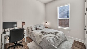 A bedroom with a bed, a desk with a chair, a TV, and two wall-mounted lamps. - Modern 4-bedroom Family Home Near Downtown Austin (Manchaca)