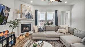 A living room with a fireplace, a sectional sofa, a coffee table, and a ceiling fan. - Modern 4-bedroom Family Home Near Downtown Austin (Manchaca)