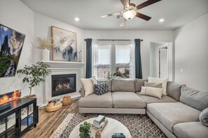 Ein Wohnzimmer mit Kamin, einem Ecksofa, einem Couchtisch und einem Deckenventilator.