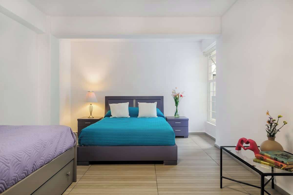 A bedroom with a bed, bedside tables, a nightstand, a window, and a small table with books and a vase.