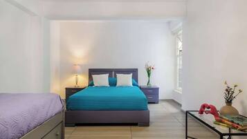 A bedroom with a bed, bedside tables, a nightstand, a window, and a small table with books and a vase.
