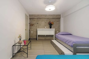 Ein Schlafzimmer mit einem Bett, einem Nachttisch, einem kleinen Schreibtisch und einem an der Wand befestigten Regal.