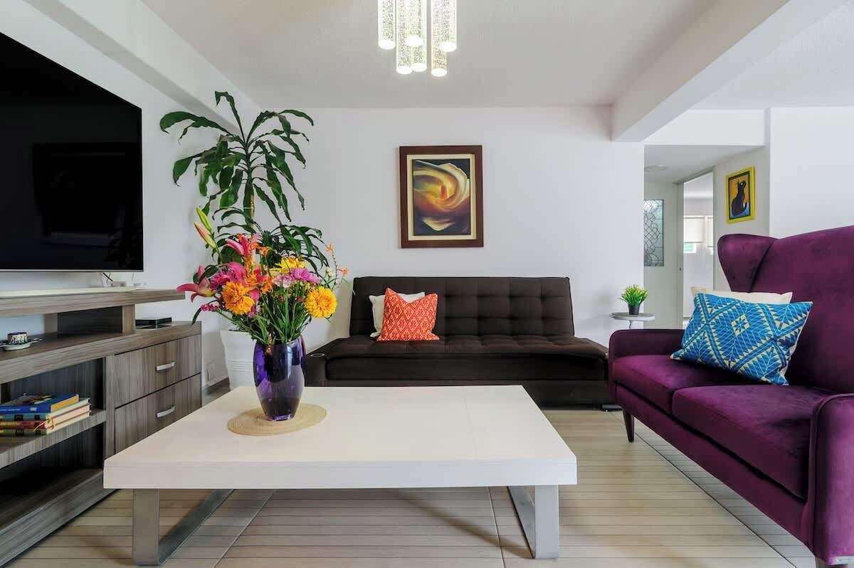 A modern living room with a flat-screen TV, a sofa, a coffee table, and a potted plant.