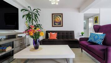 A modern living room with a flat-screen TV, a sofa, a coffee table, and a potted plant.