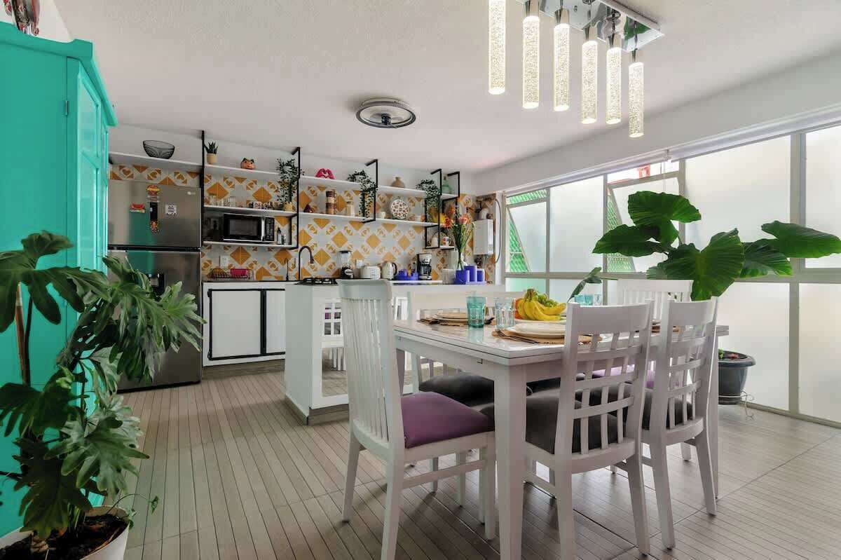 A modern kitchen with a dining area, white cabinetry, and a large window.