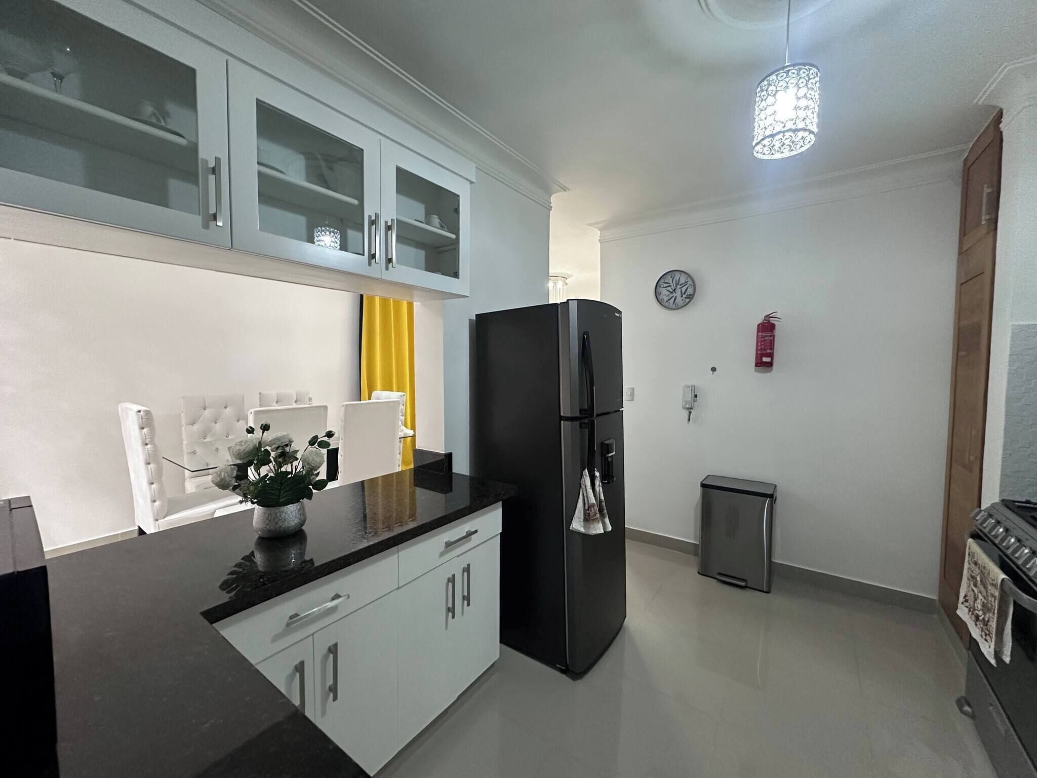 A modern kitchen with a black refrigerator, white cabinets, a yellow curtain, and a clock on the wall.