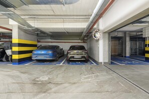 Un estacionamiento con dos autos estacionados, pilares de concreto con franjas amarillas y negras, y una señal circular en la pared.