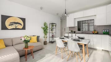 Uma sala de estar moderna com sofá, mesa de jantar e área de cozinha com armários brancos e painel de backsplash de tijolos.