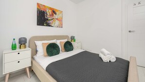 Um quarto com uma cama, mesas de cabeceira, um quadro e uma porta.