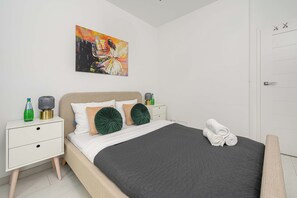 Ein Schlafzimmer mit einem Bett, Nachttischen, einem Gemälde und einer Tür.
