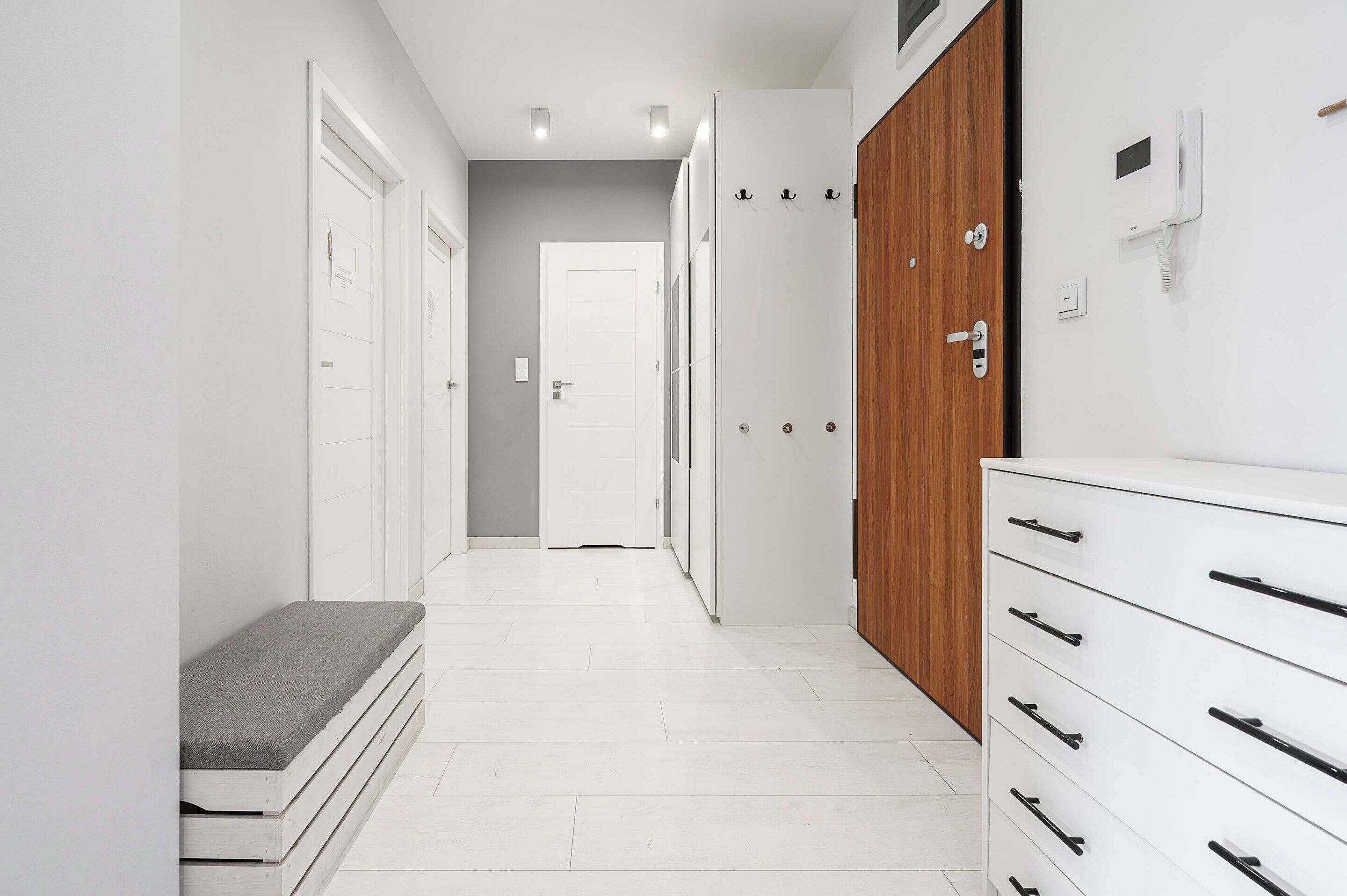 Un couloir aux murs blancs, avec une armoire en bois et un banc.