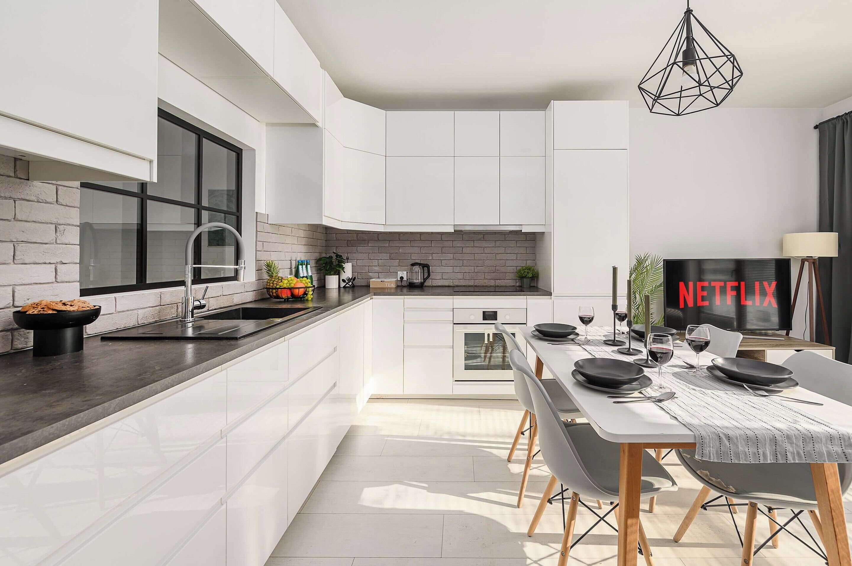 Una cocina moderna con armarios blancos, horno empotrado y un comedor con mesa para dos.