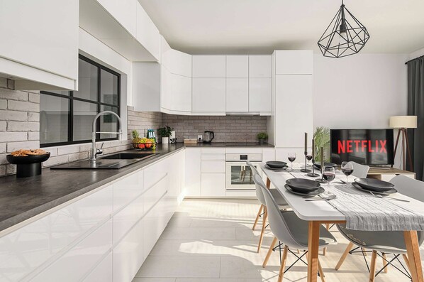 A modern kitchen with white cabinetry, a built-in oven, and a dining area with a table set for two. - Family Flat With Garden (Warsaw)