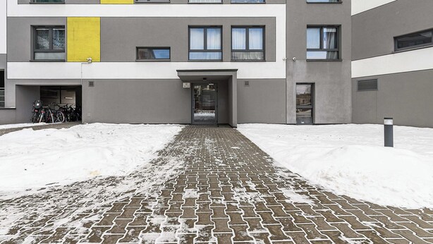 Um edifício moderno com entrada pavimentada e neve no chão.