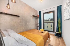A bedroom with a bed, a window, a view of buildings, a shelf, and a plant. - Home Near Warsaw Spire (Warsaw)