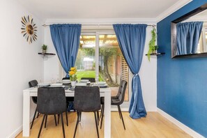Un comedor con una mesa dispuesta para cuatro, cortinas azules, una planta en maceta y un espejo colgado en la pared.